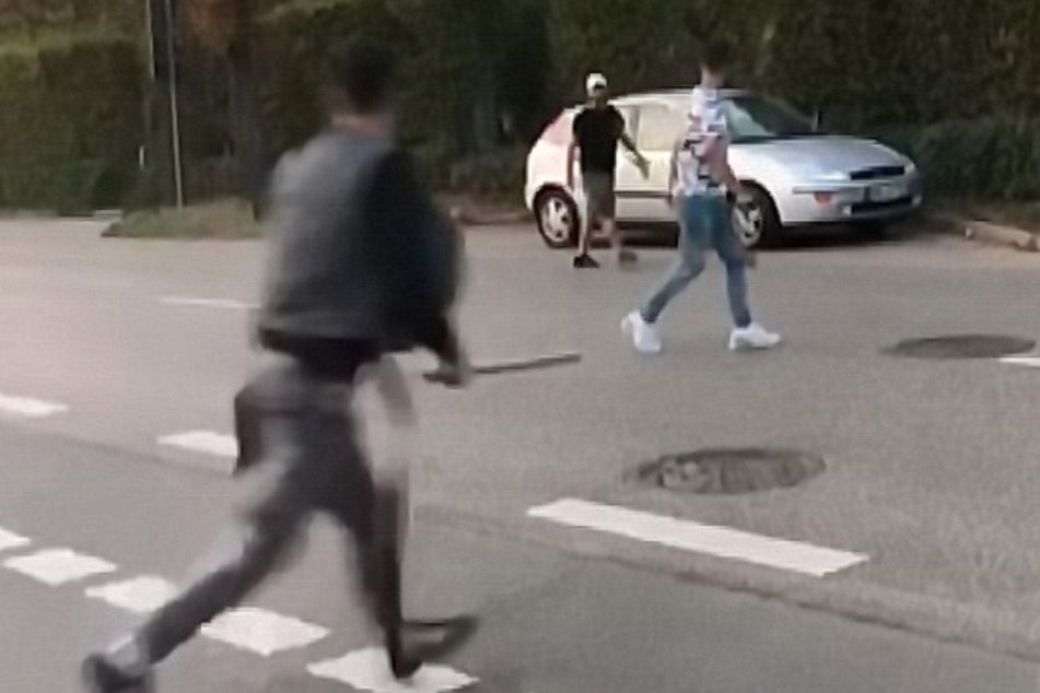 Mit einem stangenähnlichen Gegenstand läuft eine Person über die Straße.