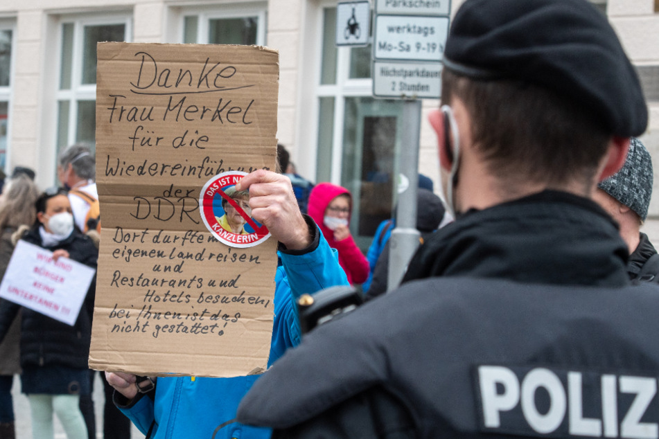 Ein Mann hält Polizisten ein Plakat gegen Bundeskanzlerin Merkel entgegen.