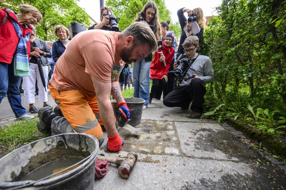 Ein Bauarbeiter setzt den Stolperstein in den Gehweg ein.