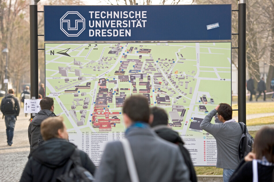 Passanten laufen an einem Gebäudeplan der Technischen Universität in Dresden vorbei.