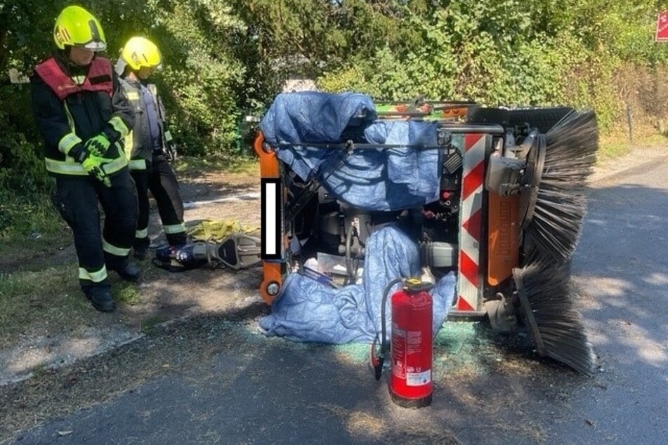 Kehrmaschine kippt um: Feuerwehr befreit Fahrer