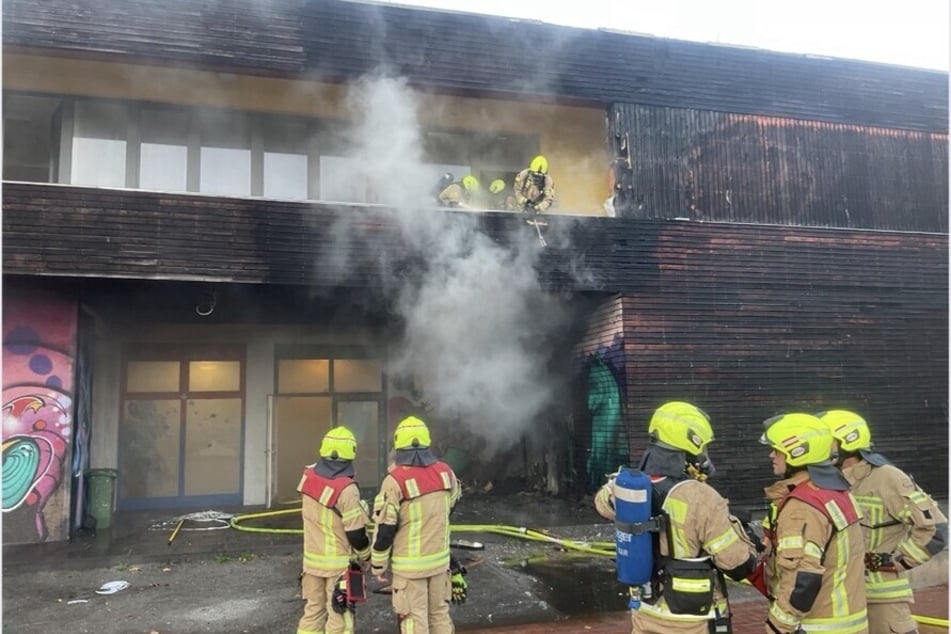 Die Einsatzkräfte löschen den Brand an der Gebäudefassade der Schule.