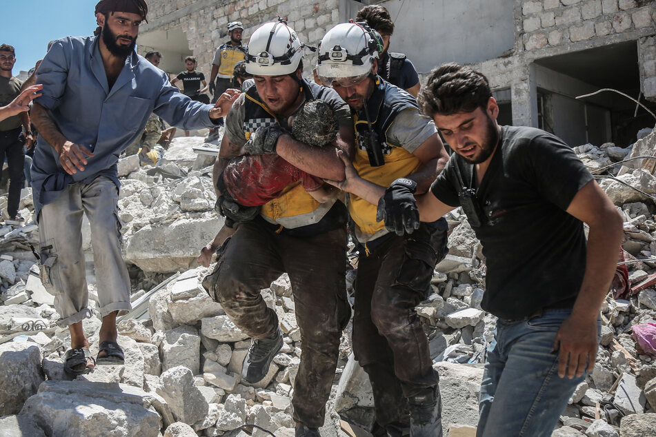 Weißhelme des syrischen Zivilschutzes tragen ein verletztes Kind aus den Trümmern eines zerstörten Gebäudes.