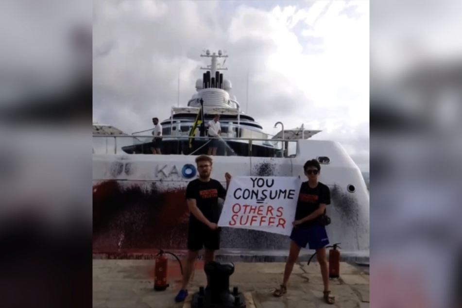 Zwei Aktivisten mit ihrer Botschaft vor der beschmierten Yacht.