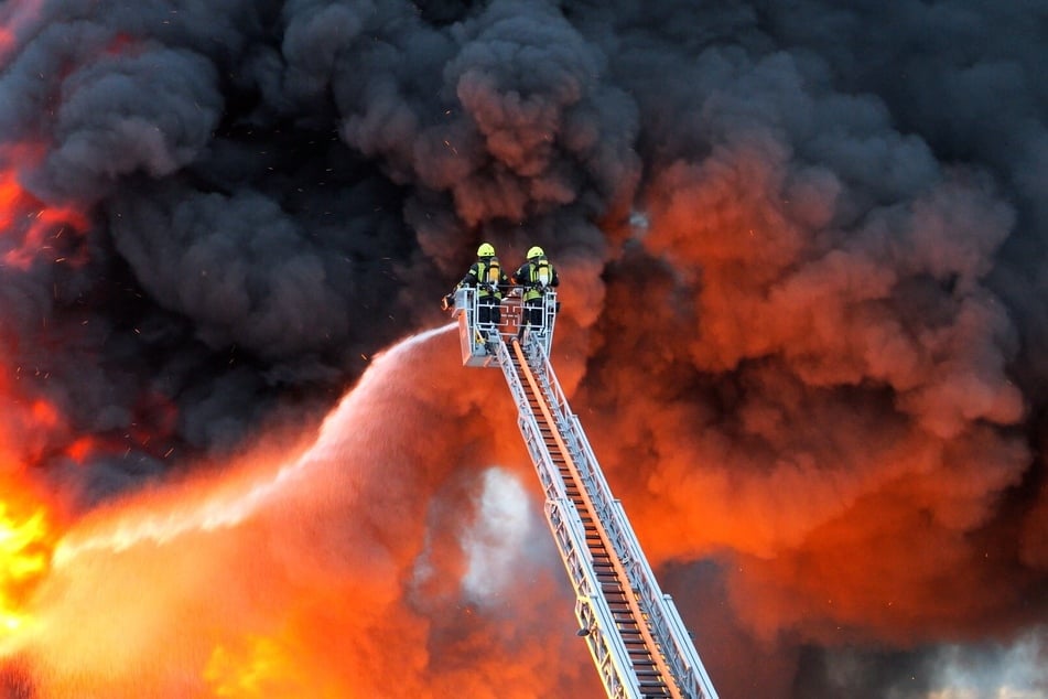 Zwei Feuerwehrleute löschen die brennende Industriehalle.