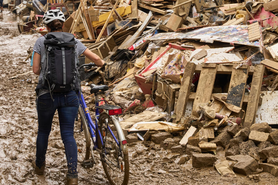 Eine Frau schiebt in Ahrweiler ihr Fahrrad durch den Schlamm. Anwohner versuchen, ihre Häuser vom Schlamm zu befreien und unbrauchbares Mobiliar nach draußen zu bringen.