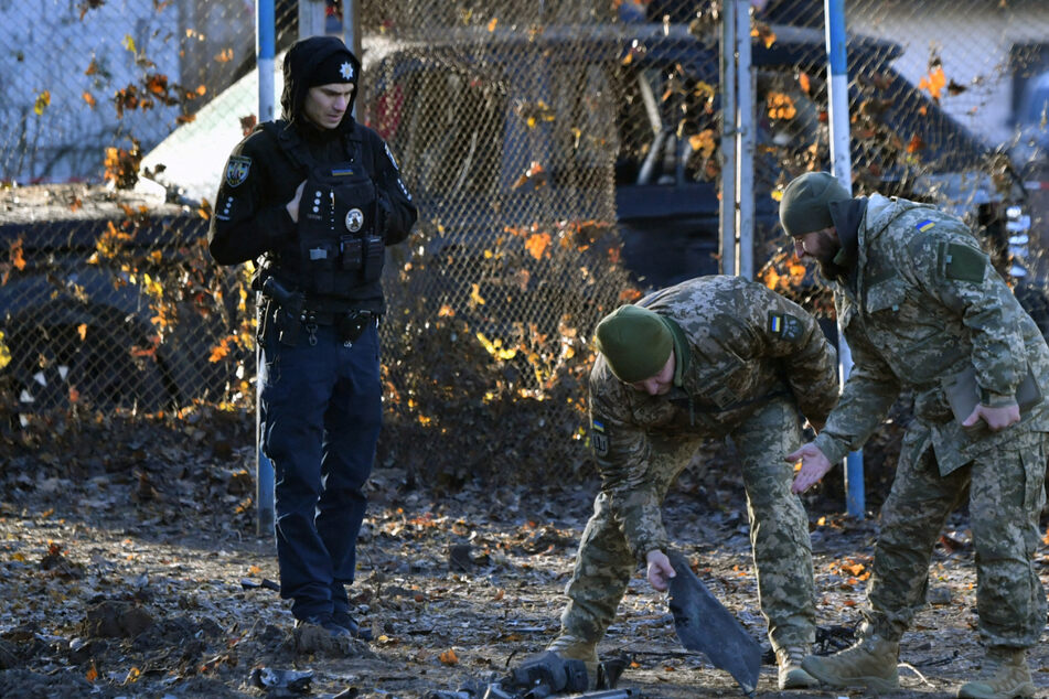 Ukrainian police and military experts collect fragments of downed Russian drone near a crater in a yard amid residential buildings in Kyiv on November 25, 2023.