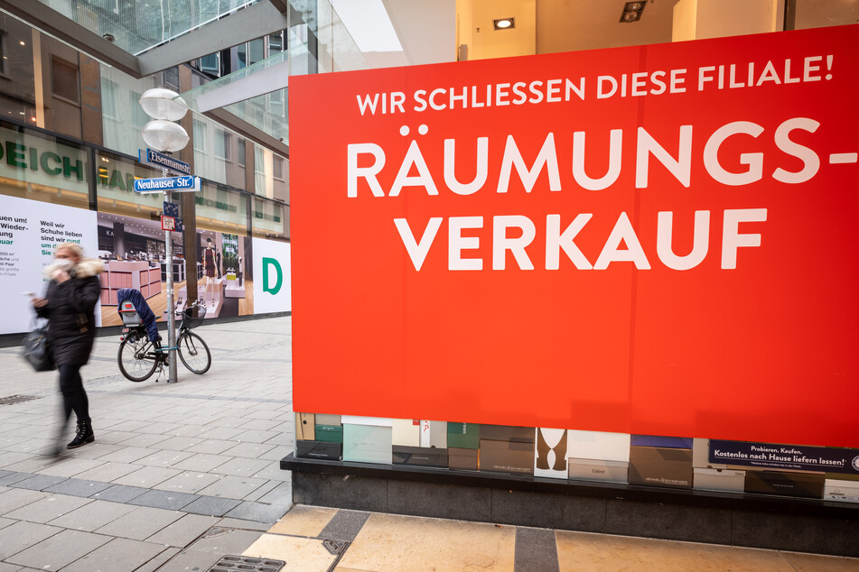 Ein Passantin läuft durch die fast leere Innenstadt von München an einem Geschäft vorbei, an dem das ein Schild mit der Aufschrift "Wir schliessen diese Filiale! - Räumungsverkauf" im Schaufenster an die Fensterscheibe geklebt wurde.