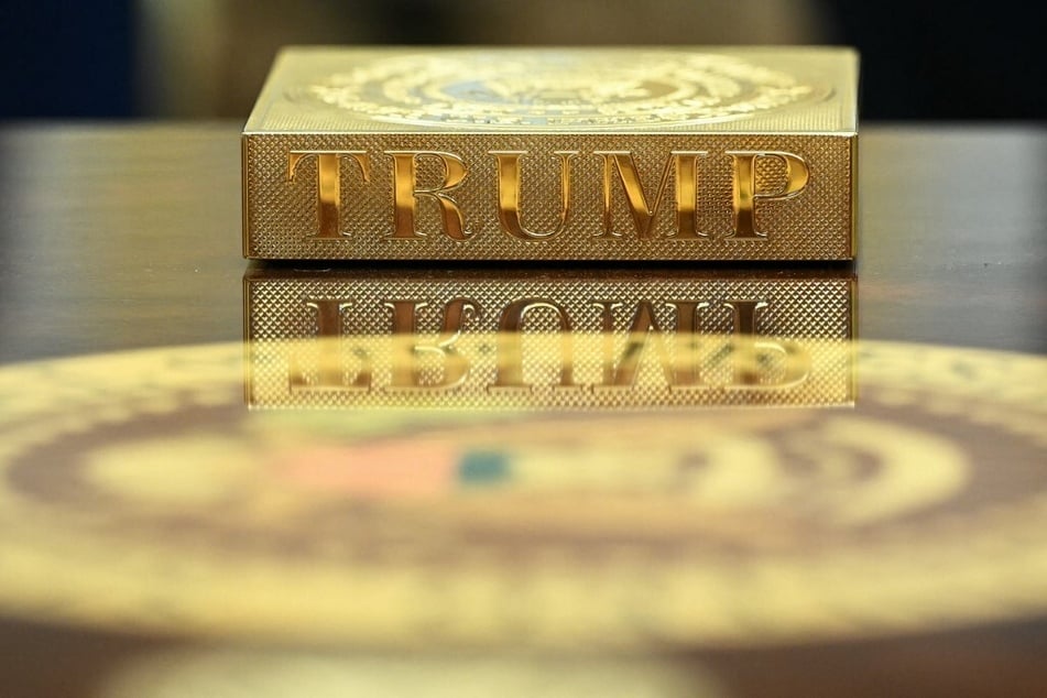 A gold coaster reading "TRUMP" sits on the table in front of President Donald Trump in the Oval Office of the White House.