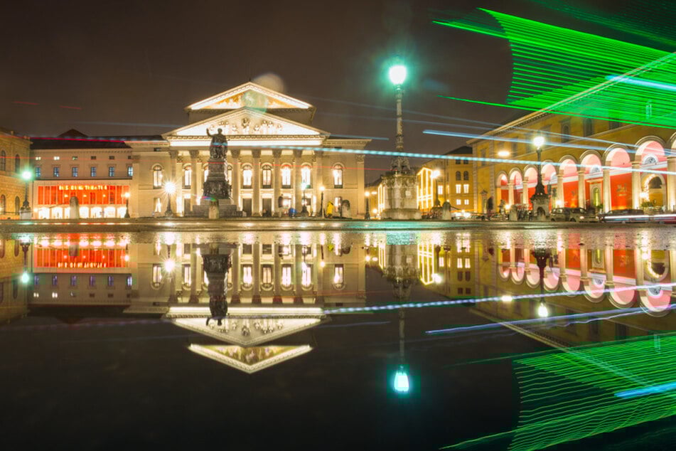 Die bayerische Staatsoper spiegelt sich in einer Pfütze auf der Münchner Residenzstrasse.