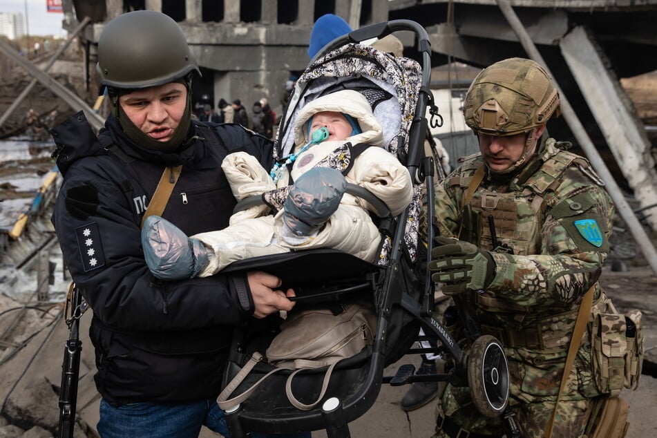 Ukrainische Soldaten tragen ein Kind in seinem Kinderwagen während einer Evakuierung in Irpin. Tausende Einwohner mussten dort ihre Häuser verlassen, da russische Truppen die Stadt bombardierten.