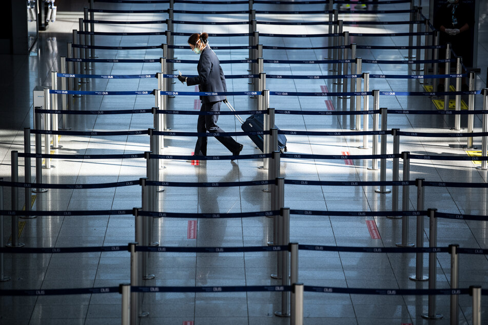 Eine Frau mit Mundschutz geht am Flughafen zu einem Check In-Schalter.