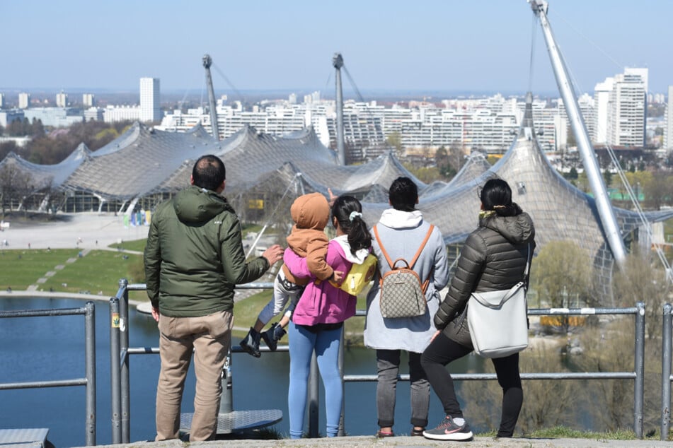 Eine Familie blickt von der Plattform des Olympiabergs in Richtung Norden auf das Zeltdach der Olympiaschwimmhalle und der Olympiahalle.