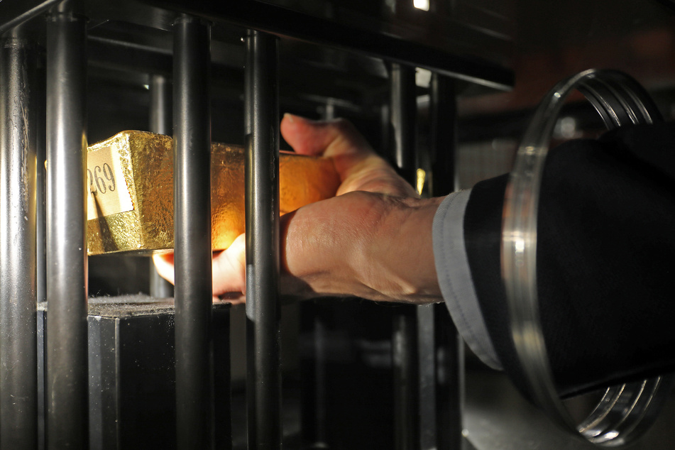 Teil der Ausstellung in Bonn: Ein Mann hebt einen 12,5 Kilo schweren Goldbarren der Deutschen Goldreserve, der in einer Vitrine gesichert ist, an.
