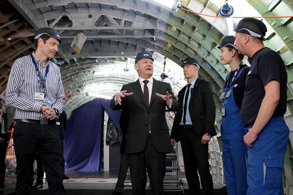Scholz (M.) spricht bei seinem Besuch der Elbe Flugzeugwerke im Inneren eines Flugzeugs mit Mitarbeitern.