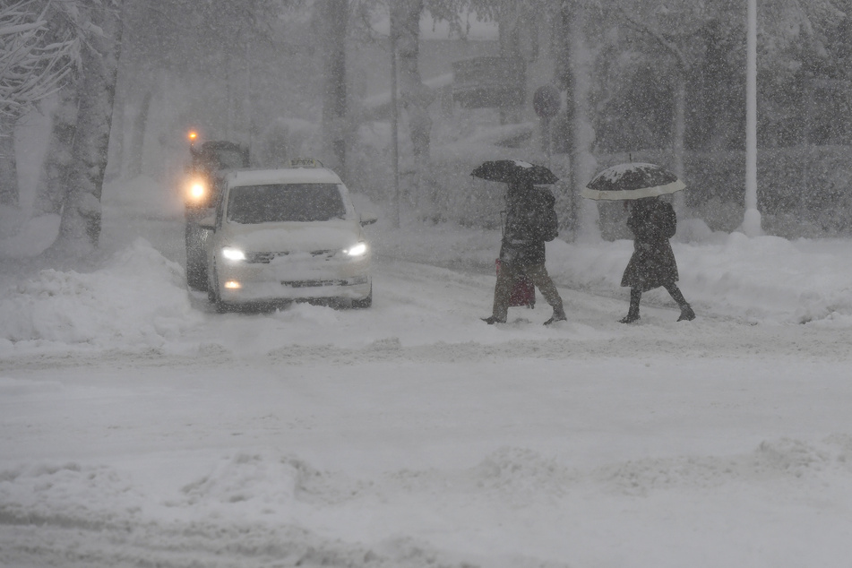 Fußgänger und Autos kämpfen sich am Donnerstag im bayrischen Garmisch-Partenkirchen durch den Schnee.