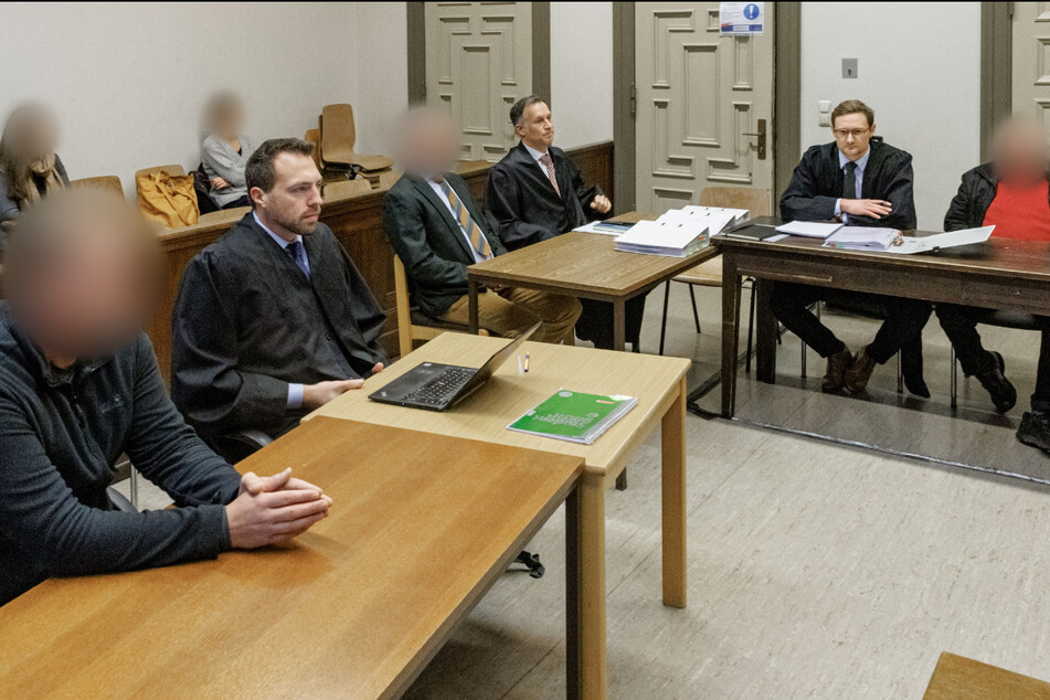 Drei Angeklagte (1., 3. und 6.vl) sitzen mit ihren Anwälten im Gerichtssaal.