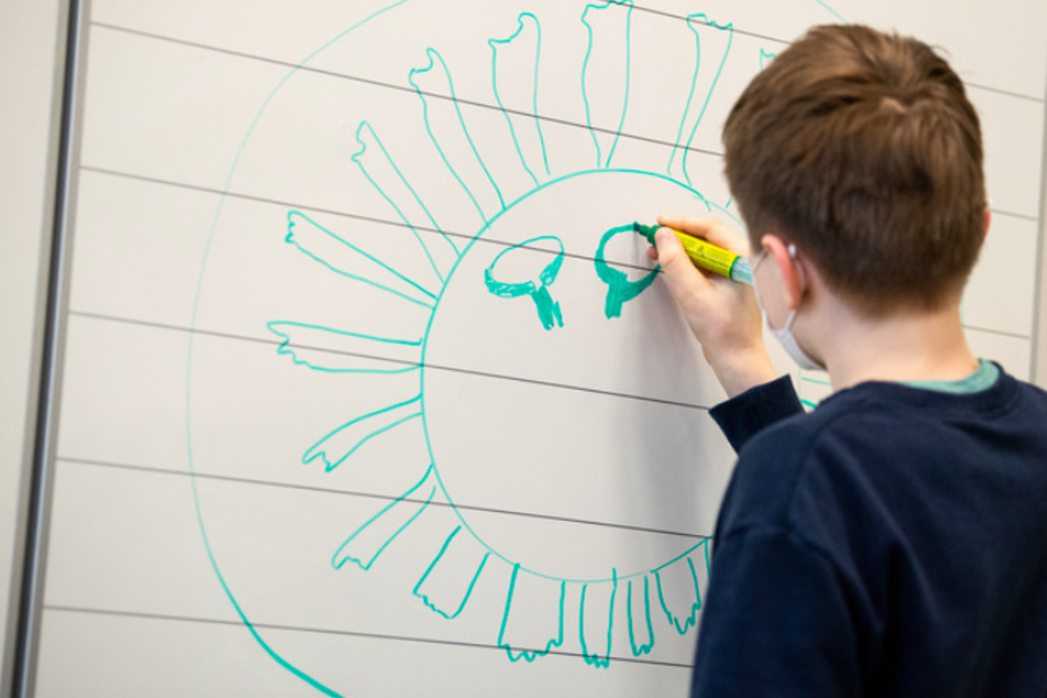 Ein Schüler zeichnet ein Coronavrus an die Tafel.
