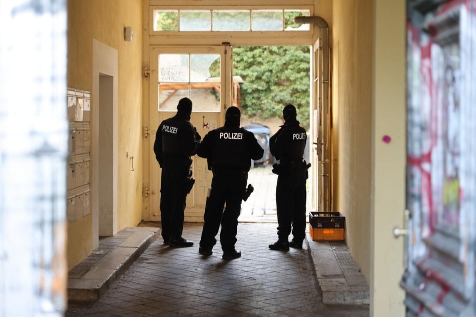 Polizisten stehen in einem Hauseingang, während ihre Kollegen nach Beweismitteln suchen.
