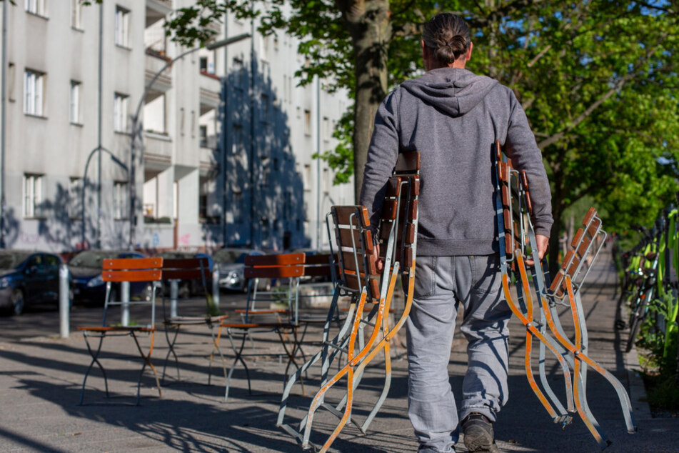 Ein Mann stellt Stühle an einem Café am Weigandufer auf. Mit dem Kaffee auf der Terrasse oder dem Weizen im Biergarten - ab Freitag heißen Gaststätten, Clubs und Freibäder in Berlin nach monatelangen coronabedingten Schließungen wieder Gäste willkommen.
