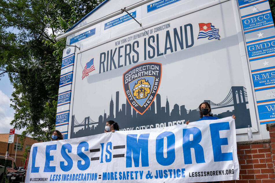 Criminal justice reform advocates hold a "Less Is More" sign at the entrance of Rikers Island.