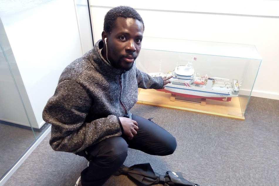 Der senegalesische Forscher Magatte Niang kniet neben einem Modell von dem Forschungsschiff Dr. Fridtjof Nansen in dem Institute of Marine Research (IMR) in Bergen.