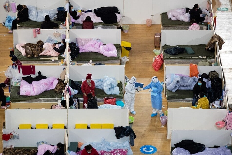 This photo taken on February 18, 2020, shows medical personnel walking among patients with mild symptoms of the Covid-19 coronavirus resting at night in a temporary hospital set up in a sports stadium in Wuhan, China.