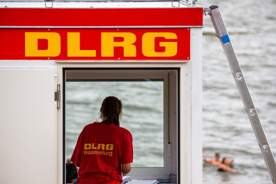 Eine Rettungsschwimmerin der DLRG (Deutsche Lebens-Rettungs-Gesellschaft) steht vor dem Fenster eines Wachturms.