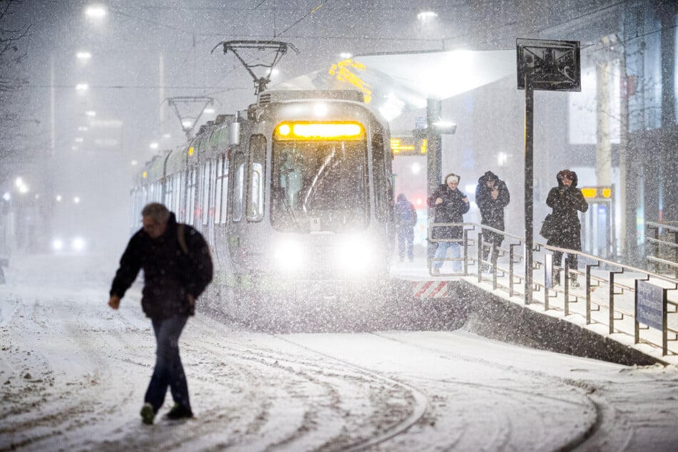 Eine Straßenbahn hält am frühen Morgen im dichten Schneefall an einer Haltestelle im Zentrum von Hannover.