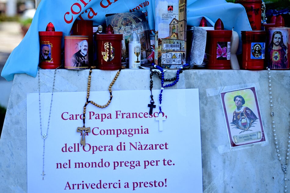 Candles and rosaries are laid at the statue of John Paul II outside the Gemelli hospital where Pope Francis is hospitalized with pneumonia, in Rome on Monday. The poster reads "Dear Pope, the company of the Work of Nazareth (ODN) prays for you. See you soon."