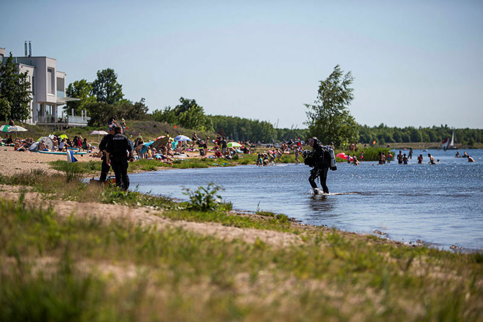 Vor Badegästen und Spaziergängern suchen Polizeitaucher am Ostufer des Cospudener Sees nach Hinweisen darauf, wie der junge Mann ums Leben kam.