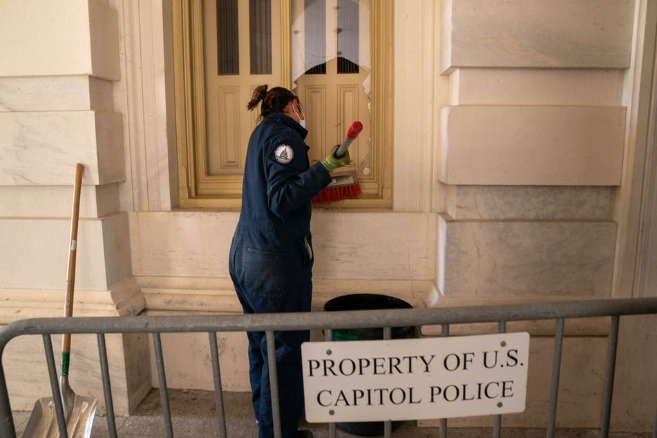 A U.S. Capitol employee cleans up glass from a broken window after Pro-Trump mobs breached the building.