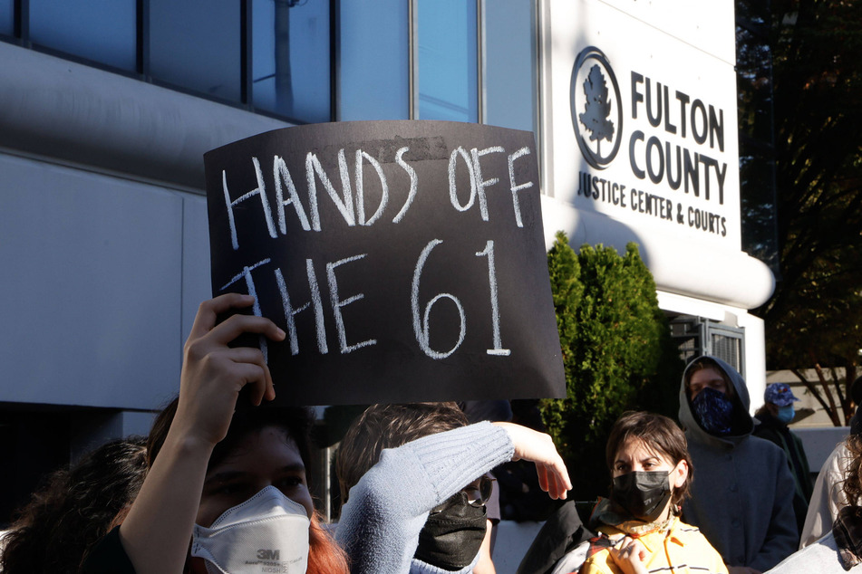 A protester raises a sign reading "Hands off the 61" during the rally against the RICO charges outside Fulton County Courthouse.