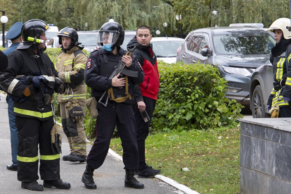 Ein bewaffneter Polizist (M) und Feuerwehrkräfte bereiten sich auf ihren Einsatz an der Staatlichen Universität in Perm vor. Zuvor hatte dort ein Mann um sich geschossen und nach Angaben des russischen Ermittlungskomitees mehrere Menschen getötet und verletzt.