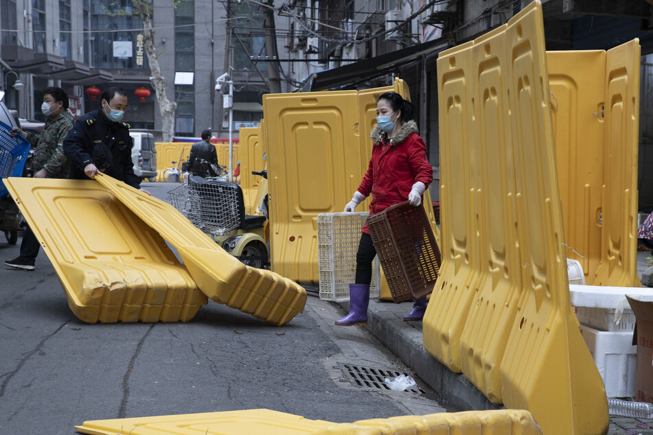 Ein Stadtarbeiter (l) beseitigt Barrieren, die dazu dienten, eine Gemeinde abzuschotten, während die Stadt Wuhan sich vor der Aufhebung der zweimonatigen Sperre langsam lockert.
