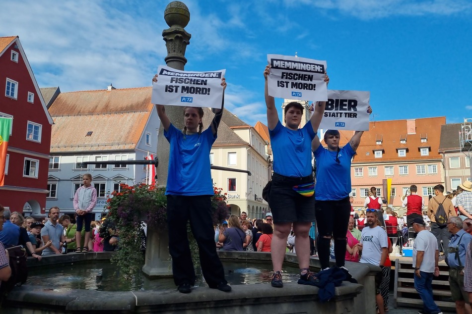 Aktivisten von PETA stehen mit Plakaten mit der Aufschrift "Fischen ist Mord" auf einem Brunnen in Memmingen.