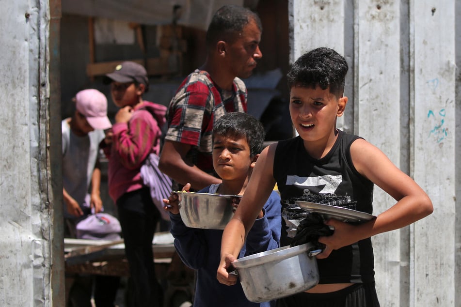 Children line up with pots to receive hot meals distributed by a charity kitchen in the Nuseirat camp for Palestinian refugees in the Central Gaza Strip on June 12, 2026.