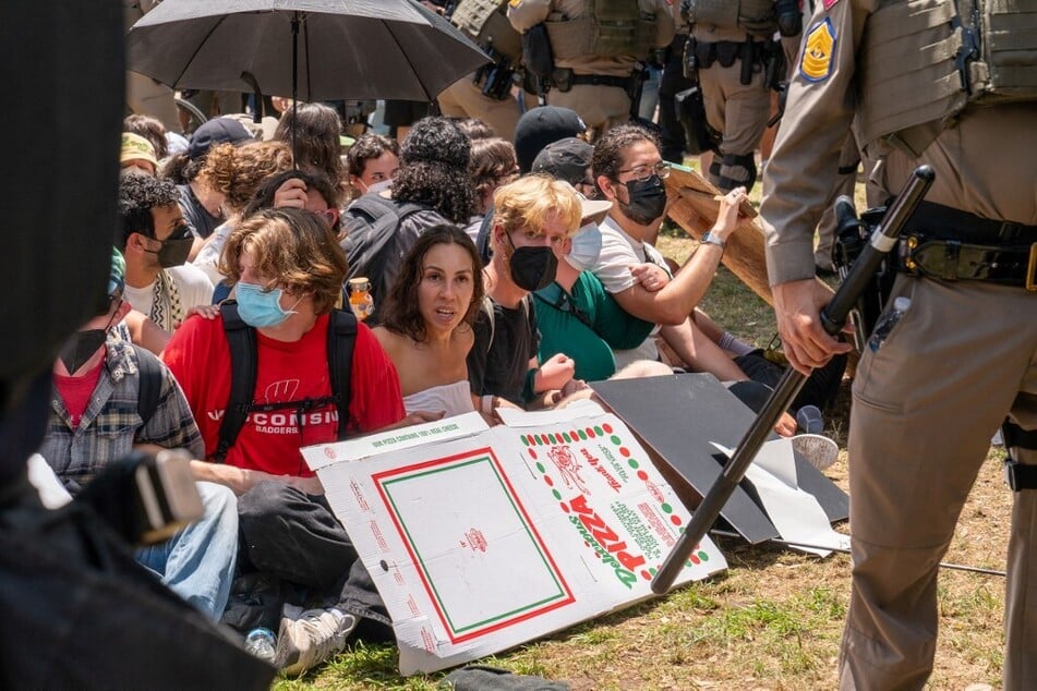 University of Texas students sit on the ground and link arms as Texas State troopers in riot gear appear to break up their demonstration.