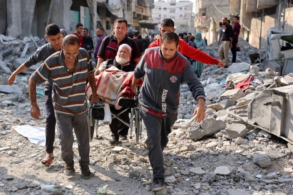 Palestinians carry an elderly man on a wheelchair through the rubble following an Israeli strike in Jabalia in the northern Gaza Strip on November 10, 2024.