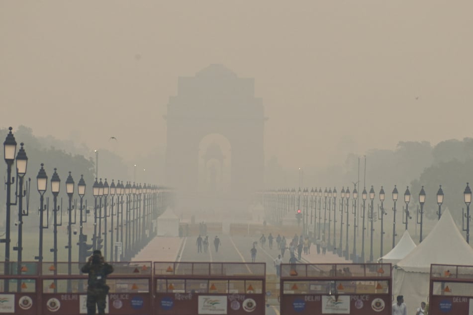 Menschen gehen inmitten des Smogs in Neu-Delhi auf einer Straße in Richtung India Gate entlang.