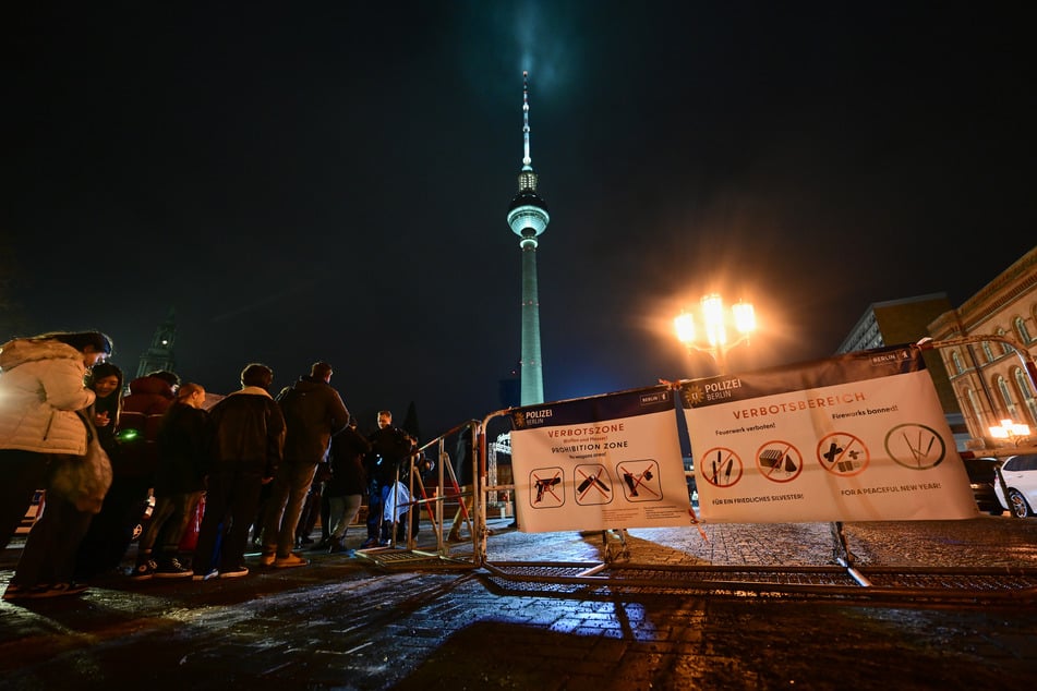 Passanten stehen an der Kontrolle eines Eingangs in die Pyrotechnikverbotszone am Alexanderplatz während der Silvesternacht.
