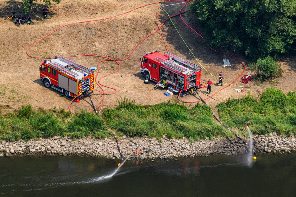 Einsatzwagen der Feuerwehr pumpen Wasser aus der Elbe.
