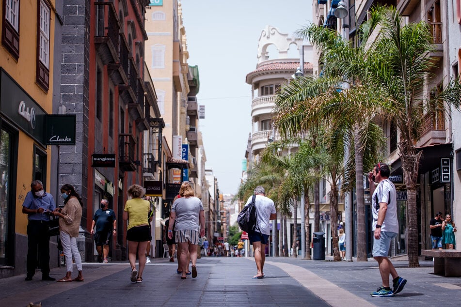 Spanien, Teneriffa: Menschen mit Masken gehen in Teneriffa eine Einkaufsstraße entlang.