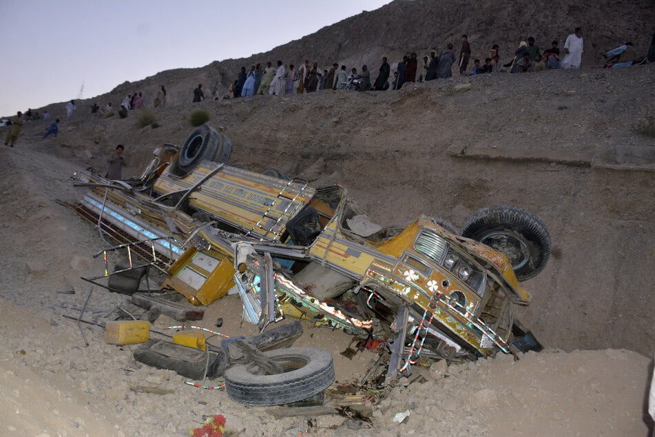 Residents gather next to the wreckage of a bus that fell into a ravine.