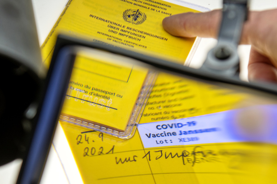 Ein Impfausweis wird mit der Lupe auf seine Echtheit hin untersucht – die Zahl der gefälschten Impfnachweise im Zusammenhang mit der Coronavirus-Pandemie hat seit dem Herbst in Hessen zugenommen. (Symbolbild)