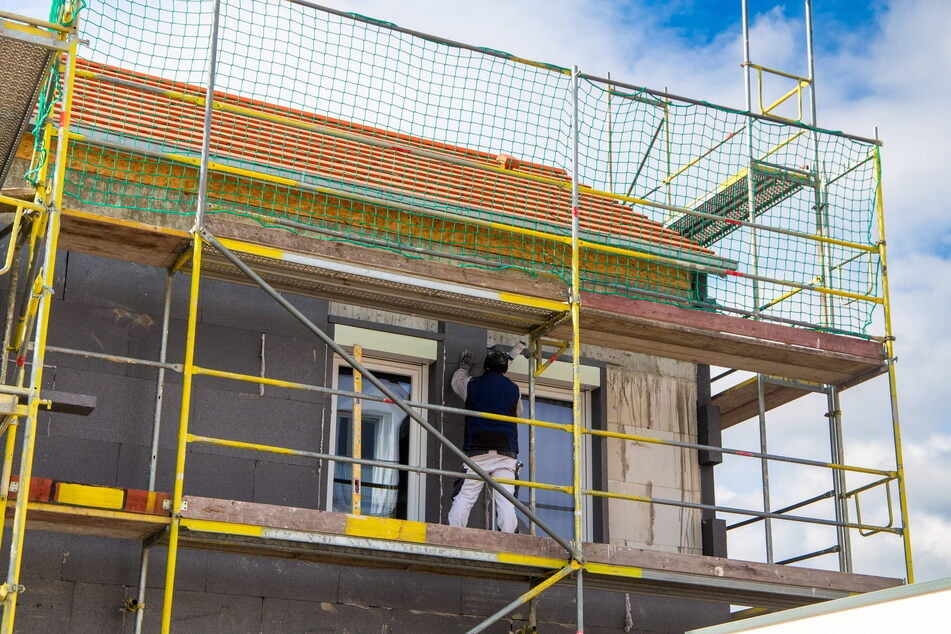 Bauarbeiter isolieren eine Hausfassade. Die Verbände fordern die Verzahnung von Wärmeplanung mit den Vorgaben für Gebäude sowie praxistaugliche Umsetzungsfristen.
