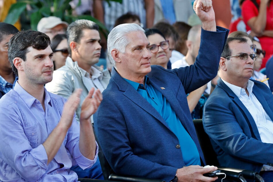 Cuba's President Miguel Diaz-Canel (c.) raises his fist next to Progressive International's general coordinator David Adler during an event at the Cuban Institute for Friendship with the Peoples in Havana on March 21, 2026.