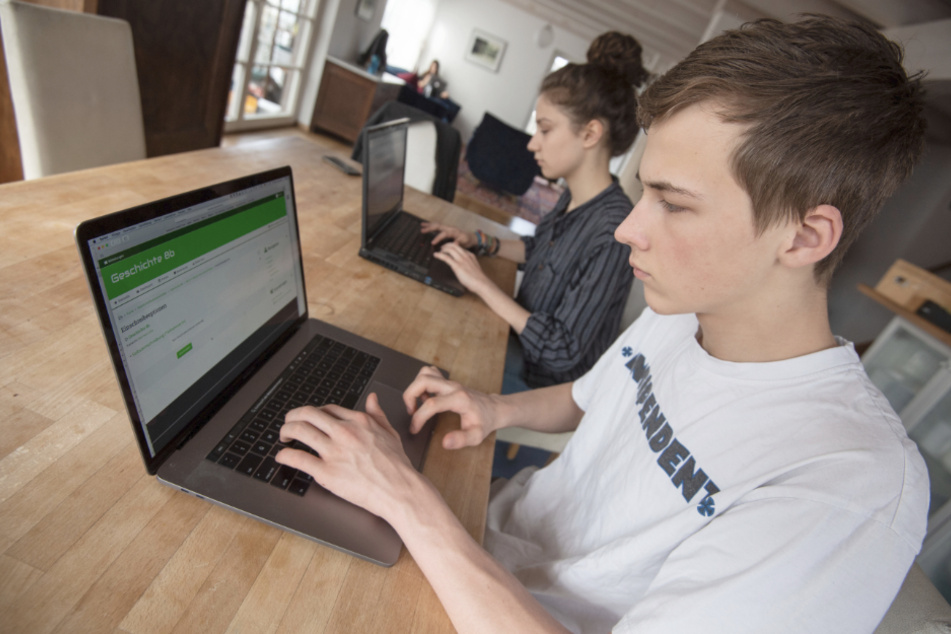 Eine Schülerin und ein Schüler arbeiten zuhause an ihren Laptops mit der Lernplattform Moodle.