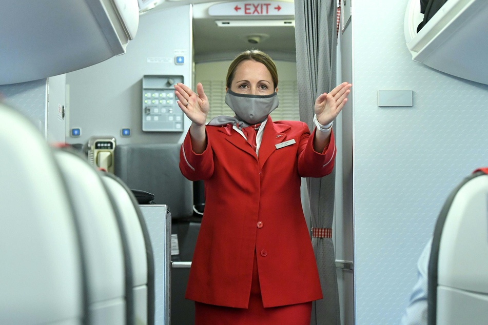 Eine Flugbegleiterin mit Mundschutz gibt Sicherheitseinweisungen in einem Flugzeug der Austrian Airlines (Archivbild).