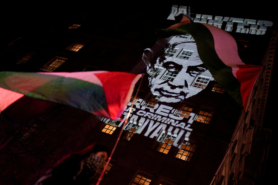 A demonstrator raises a Palestinian flag as the image calling for the arrest of Israeli Prime Minister Benjamin Netanyahu is projected on the Hay-Adams Hotel, near the White House, on February 4, 2025.